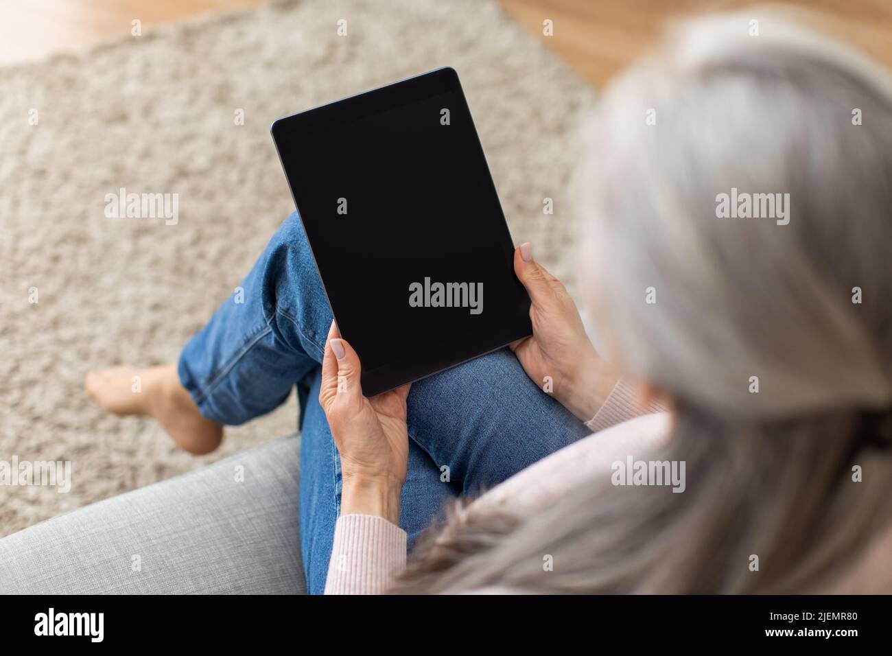 Une vieille dame européenne aux cheveux gris regarde une tablette avec écran vide, surfer sur Internet dans l'intérieur de la chambre Banque D'Images