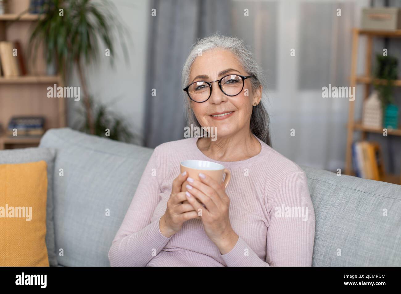 Portrait de gaie calme européenne vieille femme avec cheveux gris dans les verres tient la tasse avec boisson et profiter de temps libre Banque D'Images