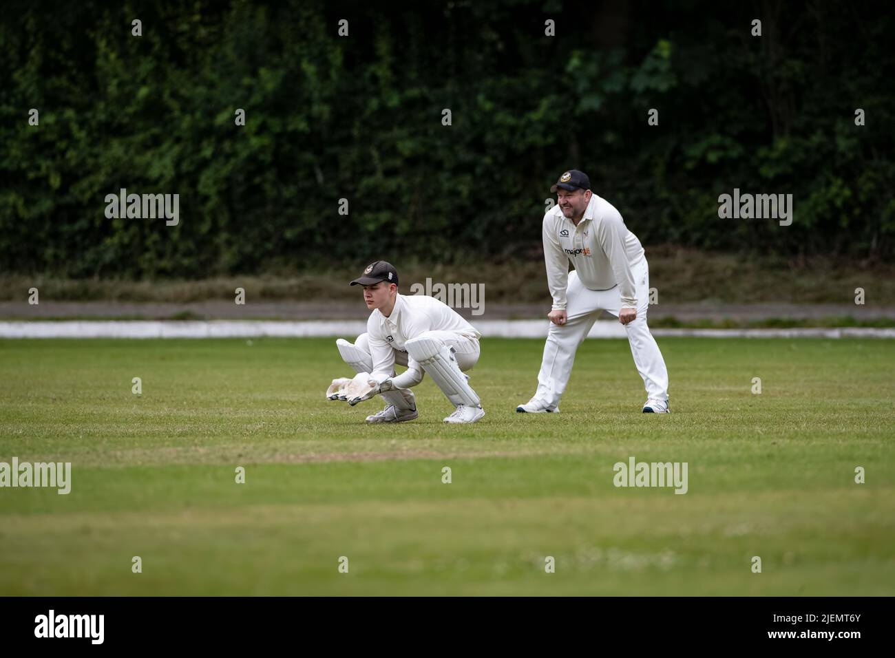 Le gardien de cricket s'est accrouillé derrière les souches avec le premier joueur de terrain lors d'un match de cricket de village de week-end à Huddersfield, dans le West Yorkshire, en Angleterre Banque D'Images