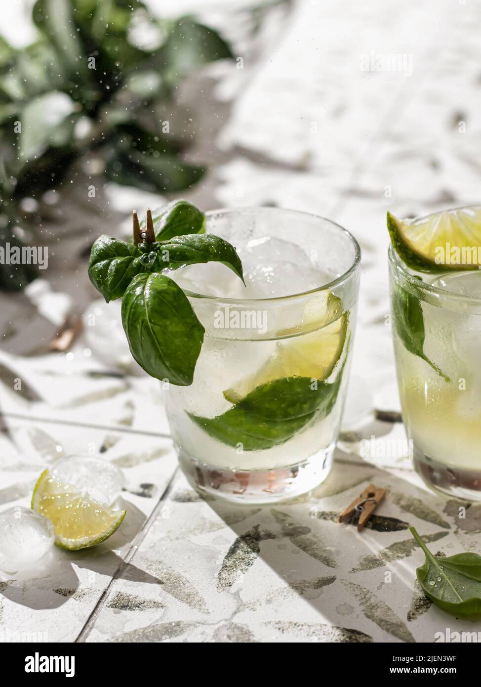 Deux cocktails d'été avec citron vert et basilic dans des verres gros plan sur carreaux blancs imprimés. Orientation verticale Banque D'Images