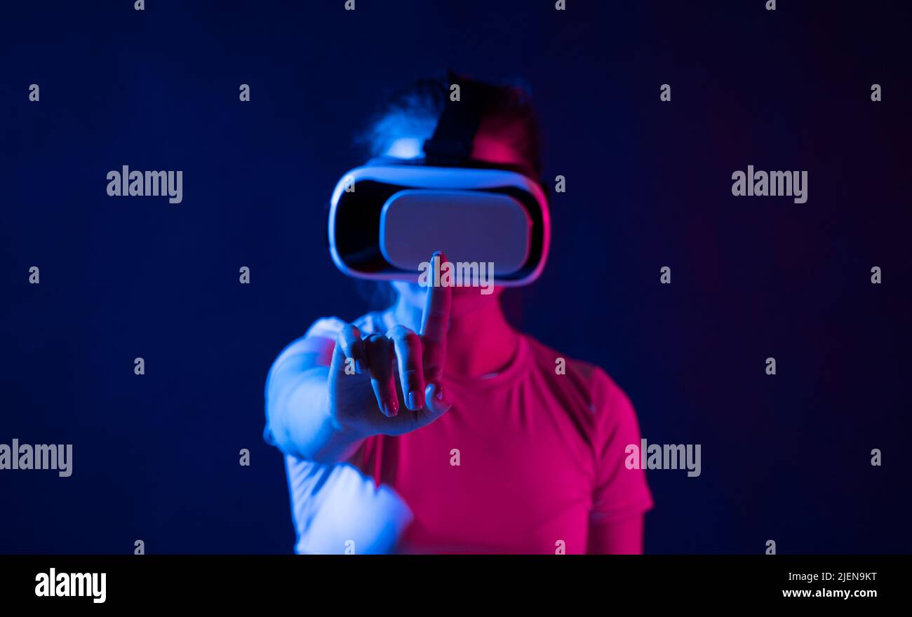 Concept de technologie métaverse. Femme avec des lunettes de réalité virtuelle VR essayant de toucher quelque chose avec un doigt. Style de vie futuriste. Banque D'Images