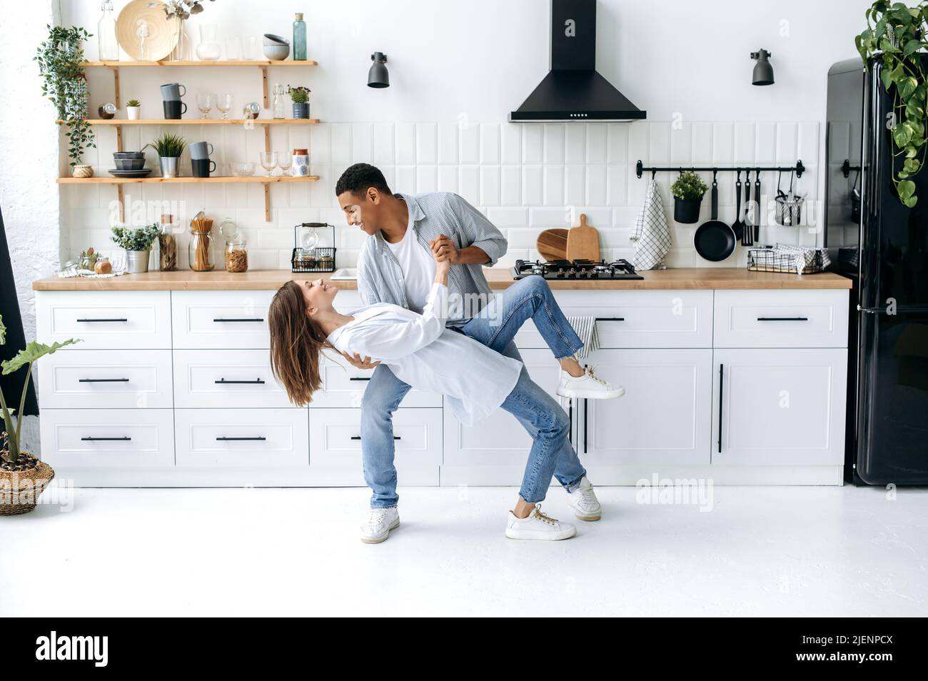 Un jeune couple heureux moderne amoureux, jeunes mariés, élégamment habillés, dansez ensemble à leur musique préférée à la maison dans la cuisine avec intérieur élégant, sourire, appréciant de passer du temps les uns avec les autres Banque D'Images