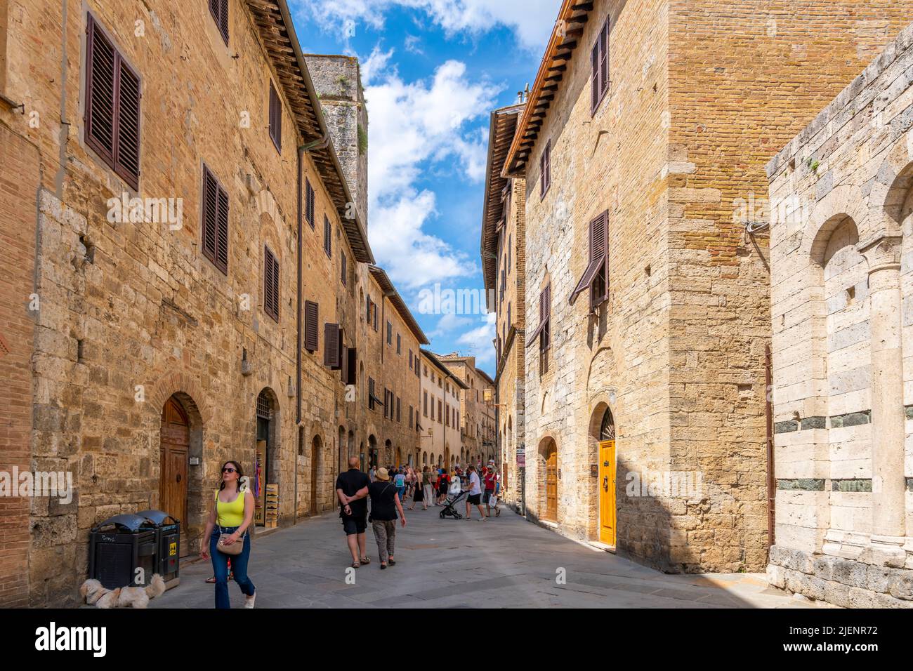 Les touristes marchent dans l'étroite rue piétonne principale remplie de boutiques et de cafés à travers la ville médiévale de colline de San Gimignano, en Italie, dans la région de Toscane. Banque D'Images