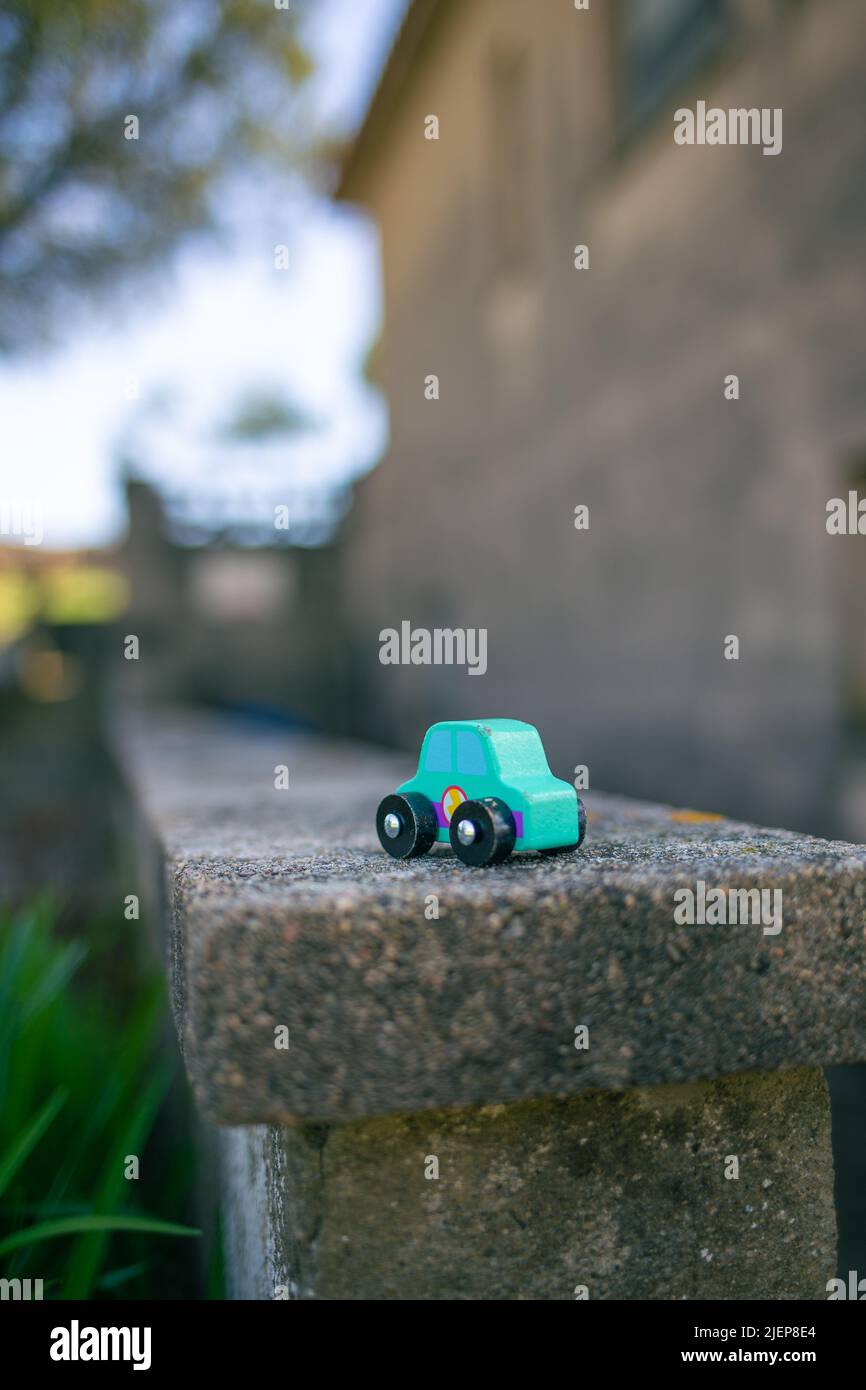 Petite voiture en bois de jouet vert isolée sur une scène urbaine extérieure sur un mur de pierre Banque D'Images