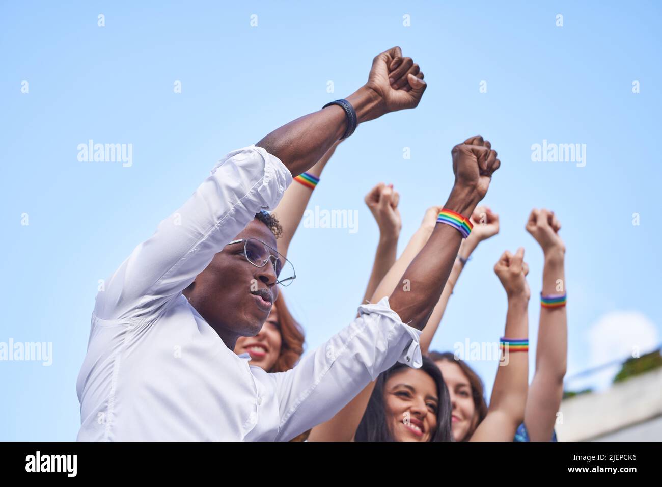 Groupe de personnes multiraciales qui élèvent des poings avec des bracelets de drapeau arc-en-ciel LGBT en plein air. Concept de diversité, d'égalité et d'unité. Banque D'Images