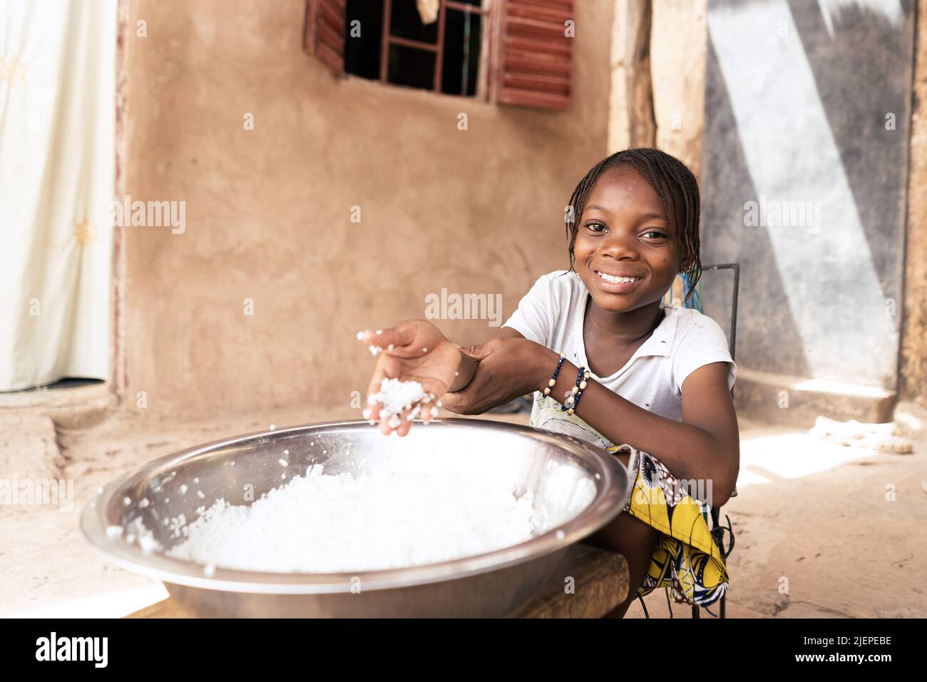 Petite fille africaine radieuse devant un plat géant appréciant son simple déjeuner fait de riz blanc bouilli Banque D'Images