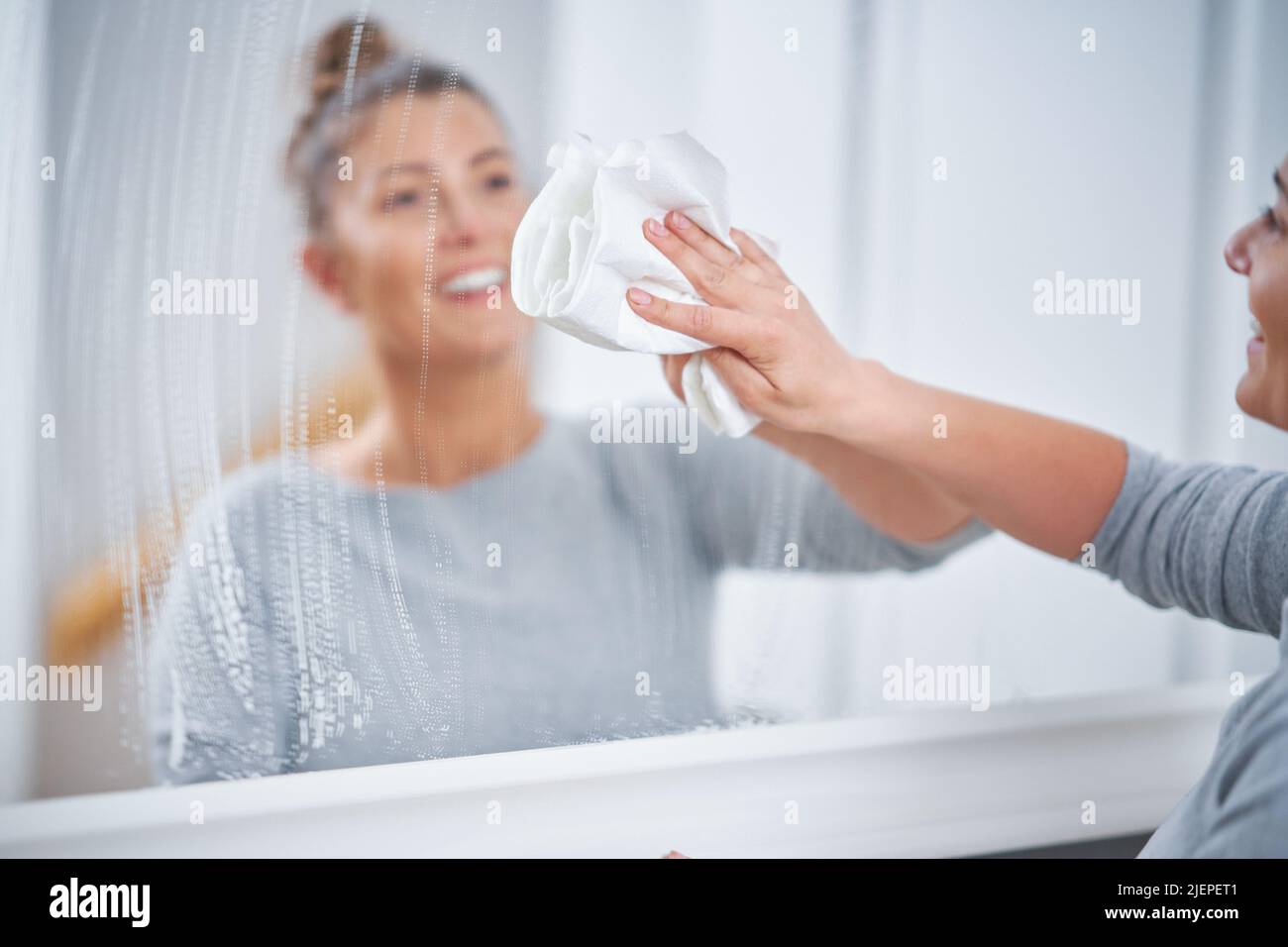 Photo de la jeune femme nettoyant miroir fenêtre Banque D'Images