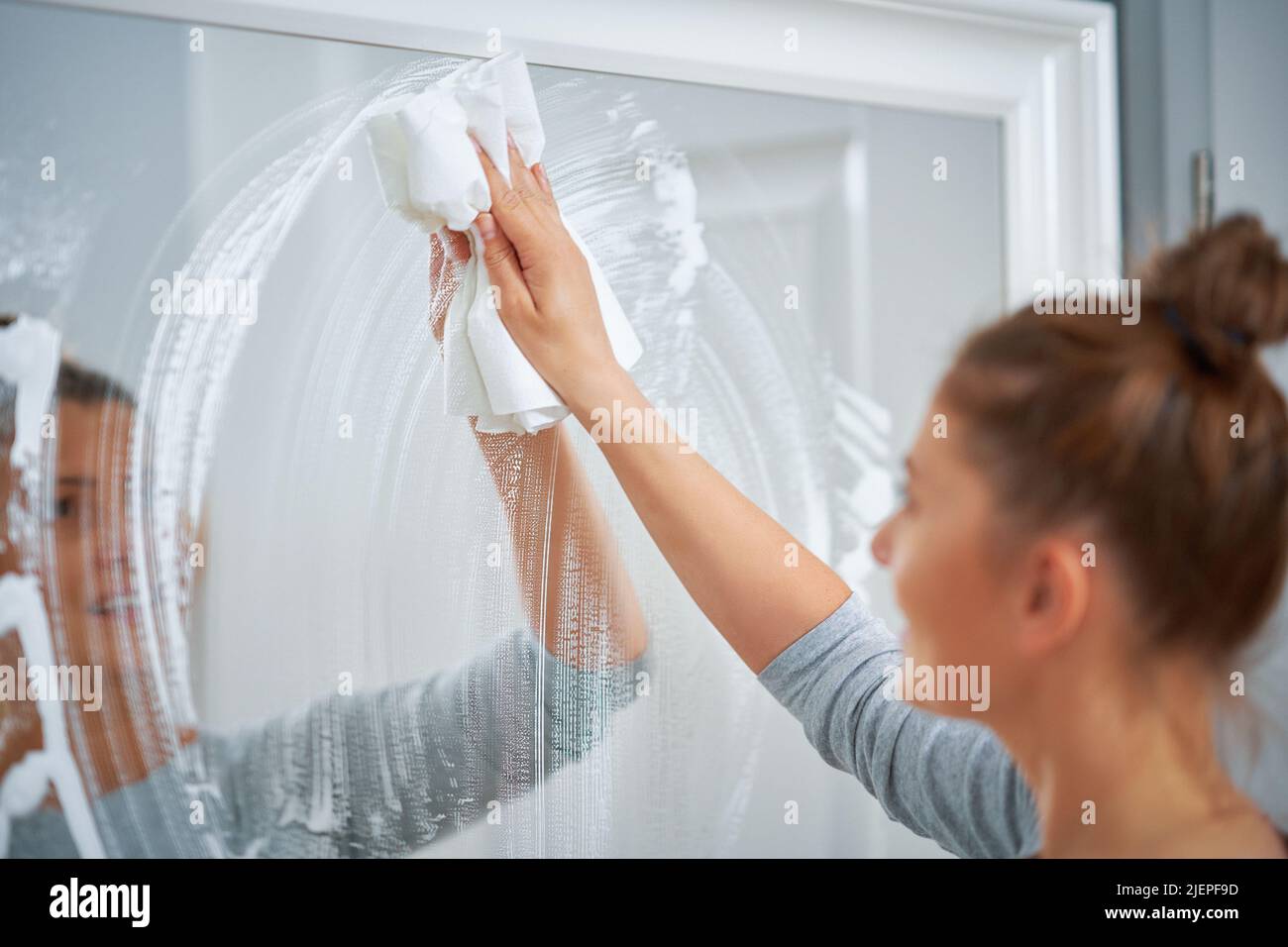 Photo de la jeune femme nettoyant miroir fenêtre Banque D'Images