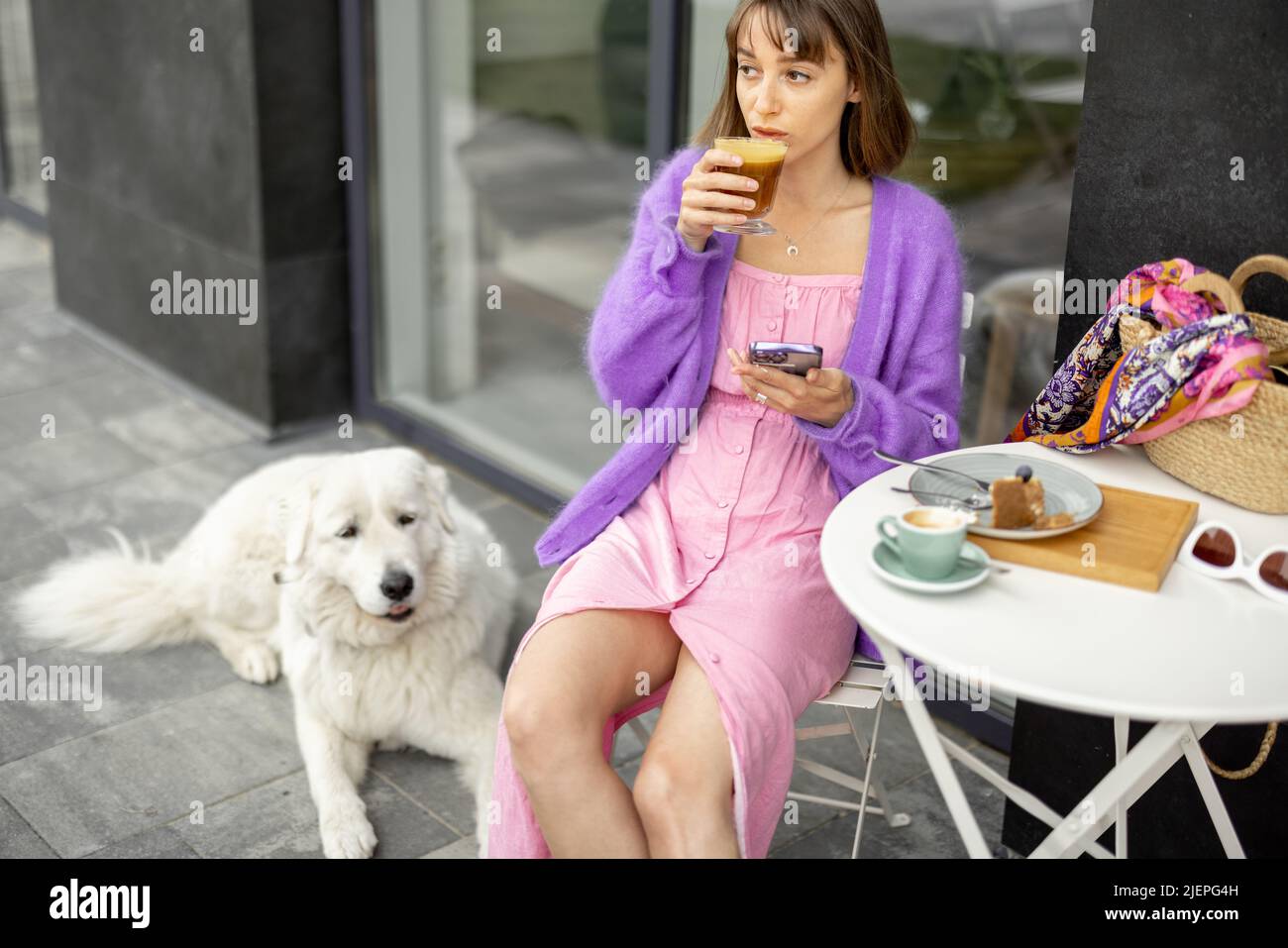 Elle est assise avec son adorable chien blanc au café dans une rue Banque D'Images