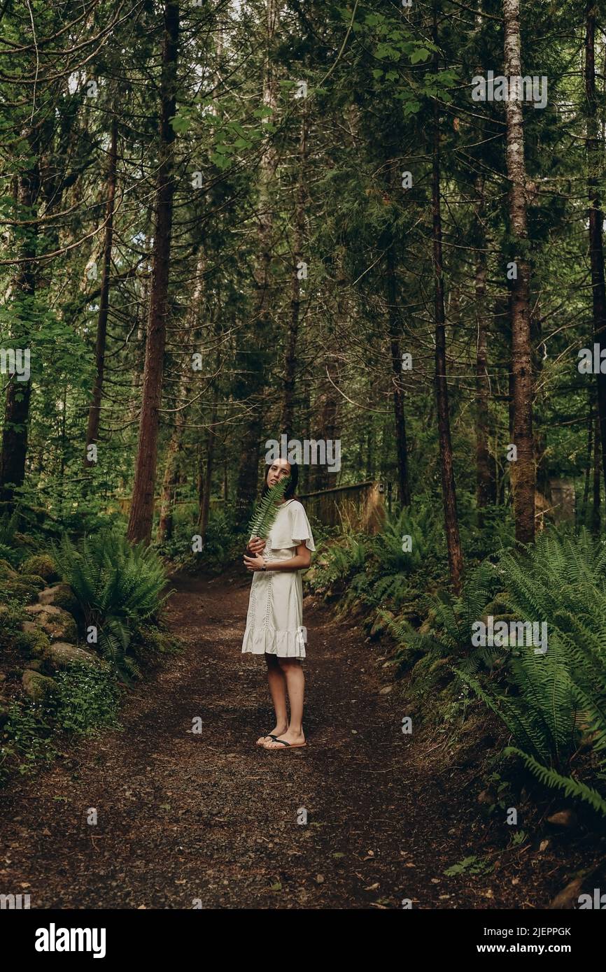 Belle jeune femme avec la fougères dans les mains sur le chemin à travers la forêt verte Banque D'Images