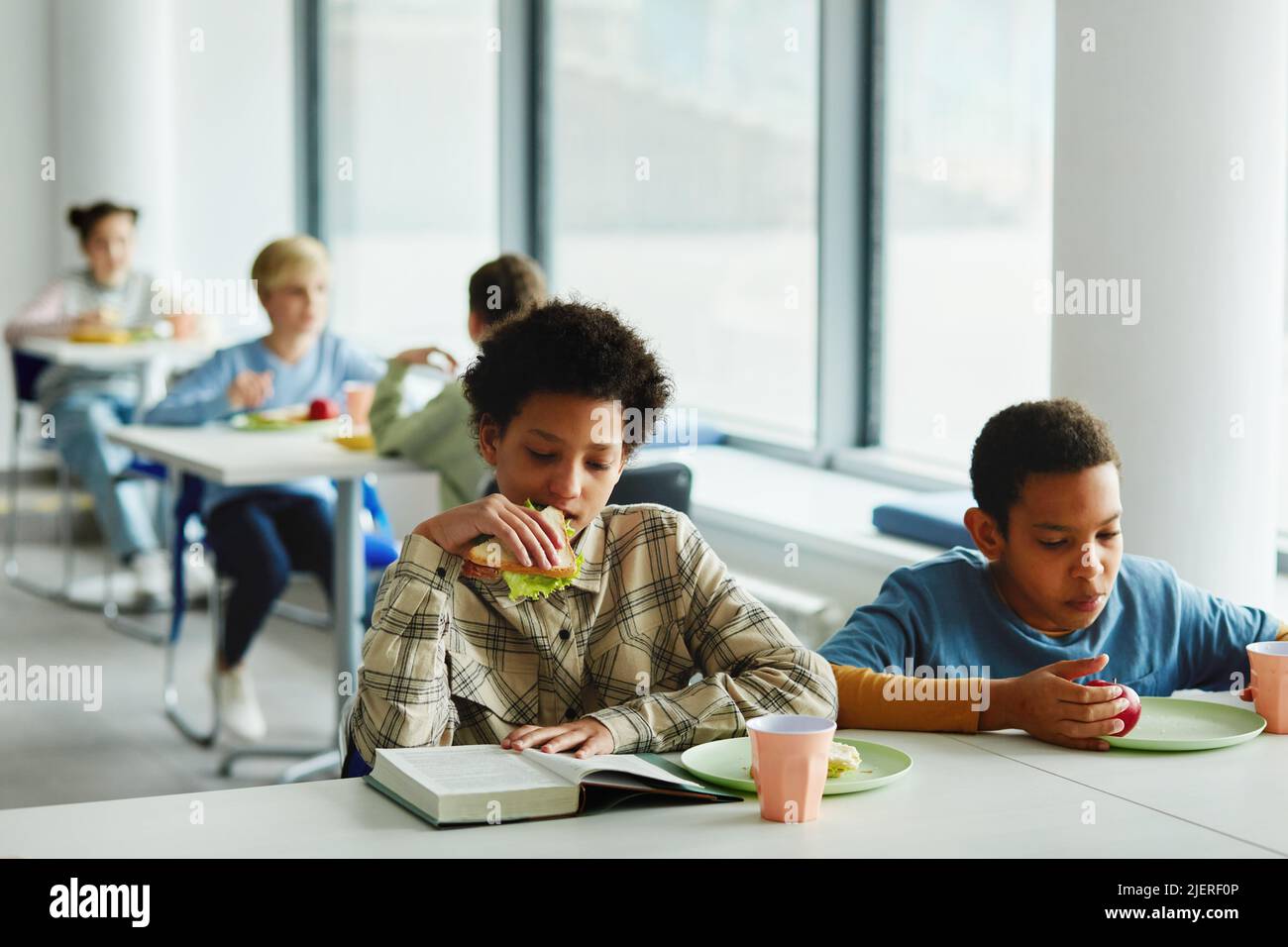 Portrait des écoliers à la pause déjeuner, se concentrer sur les jeunes afro-américaines manger sandwich et lire livre, copier espace Banque D'Images