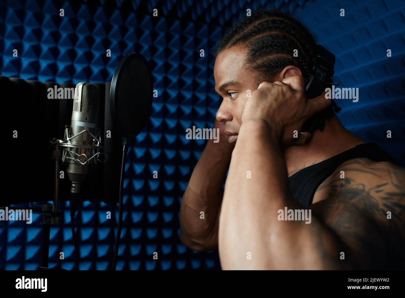 Gros plan du beau jeune chanteur noir debout devant la chanson de chant du microphone dans le studio d'enregistrement Banque D'Images
