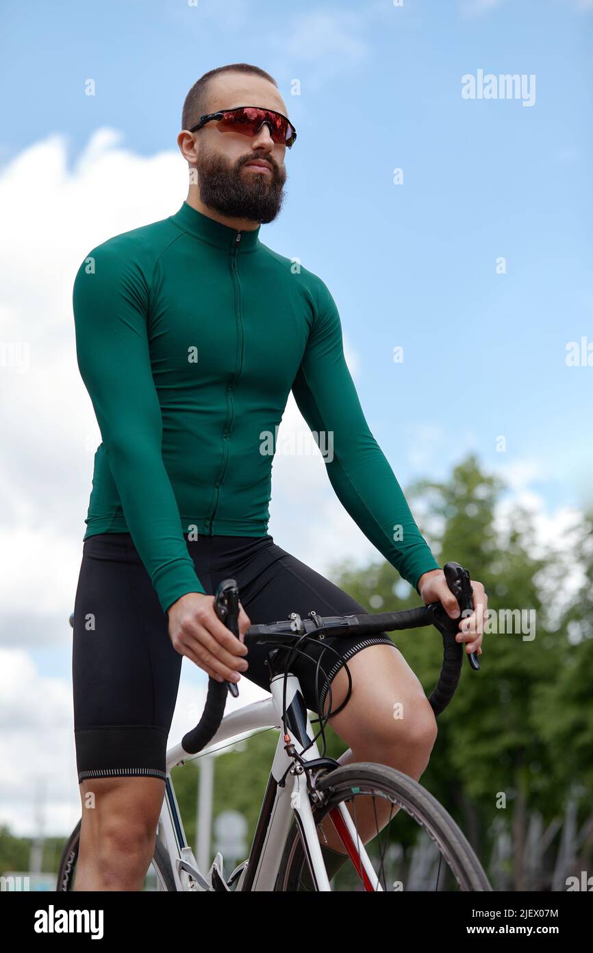 Homme dans des lunettes de soleil vitesse le long de la route sur un fond de parc d'été. Homme avec un vélo passe-temps manèges dans le parc. Banque D'Images