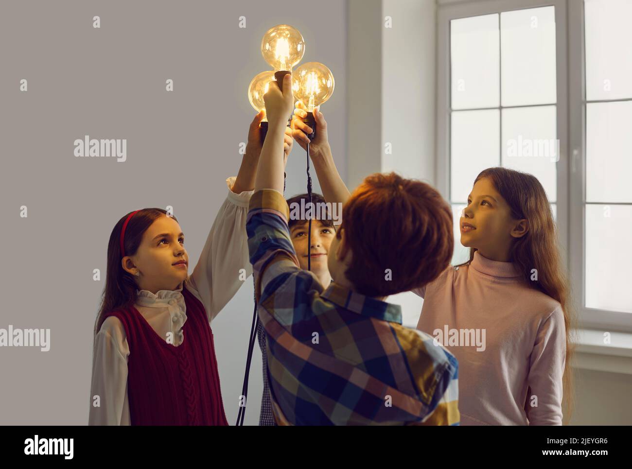 Des enfants intelligents se tenant ensemble en connectant une ampoule lumineuse en studio Banque D'Images