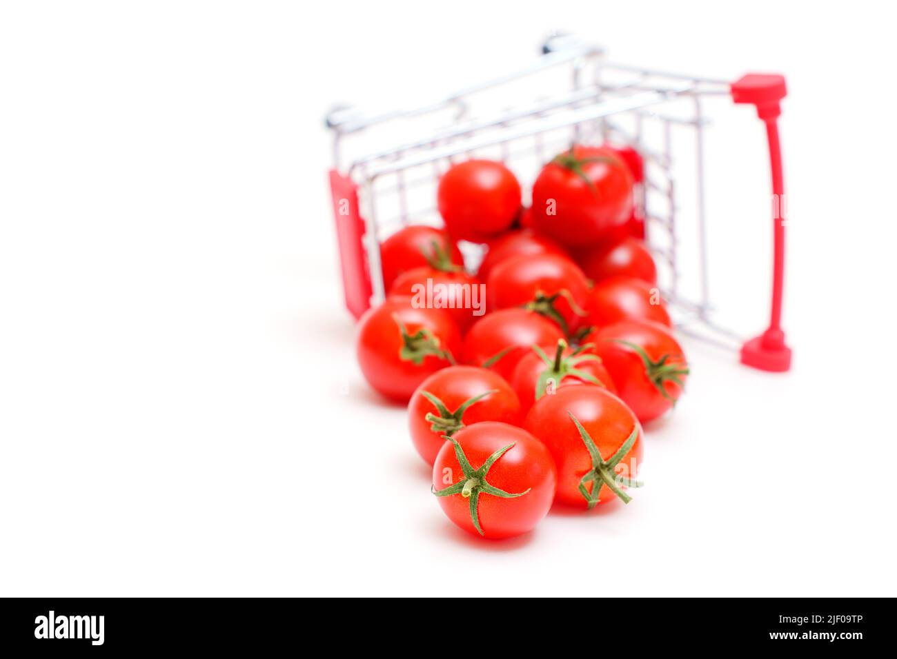 Chariot de supermarché miniature renversé avec tomates cocktail fraîches isolées sur blanc. Banque D'Images