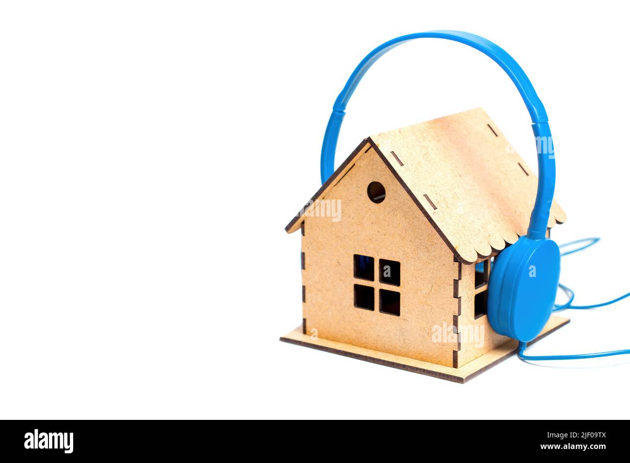 Casque bleu mis sur un modèle de maison en bois miniature isolé sur fond blanc. Concept de bruit domestique et d'isolation acoustique. Banque D'Images