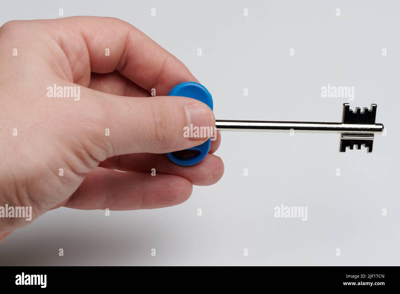 Clé métallique argentée dans les doigts isolés sur l'arrière-plan du studio macro Banque D'Images