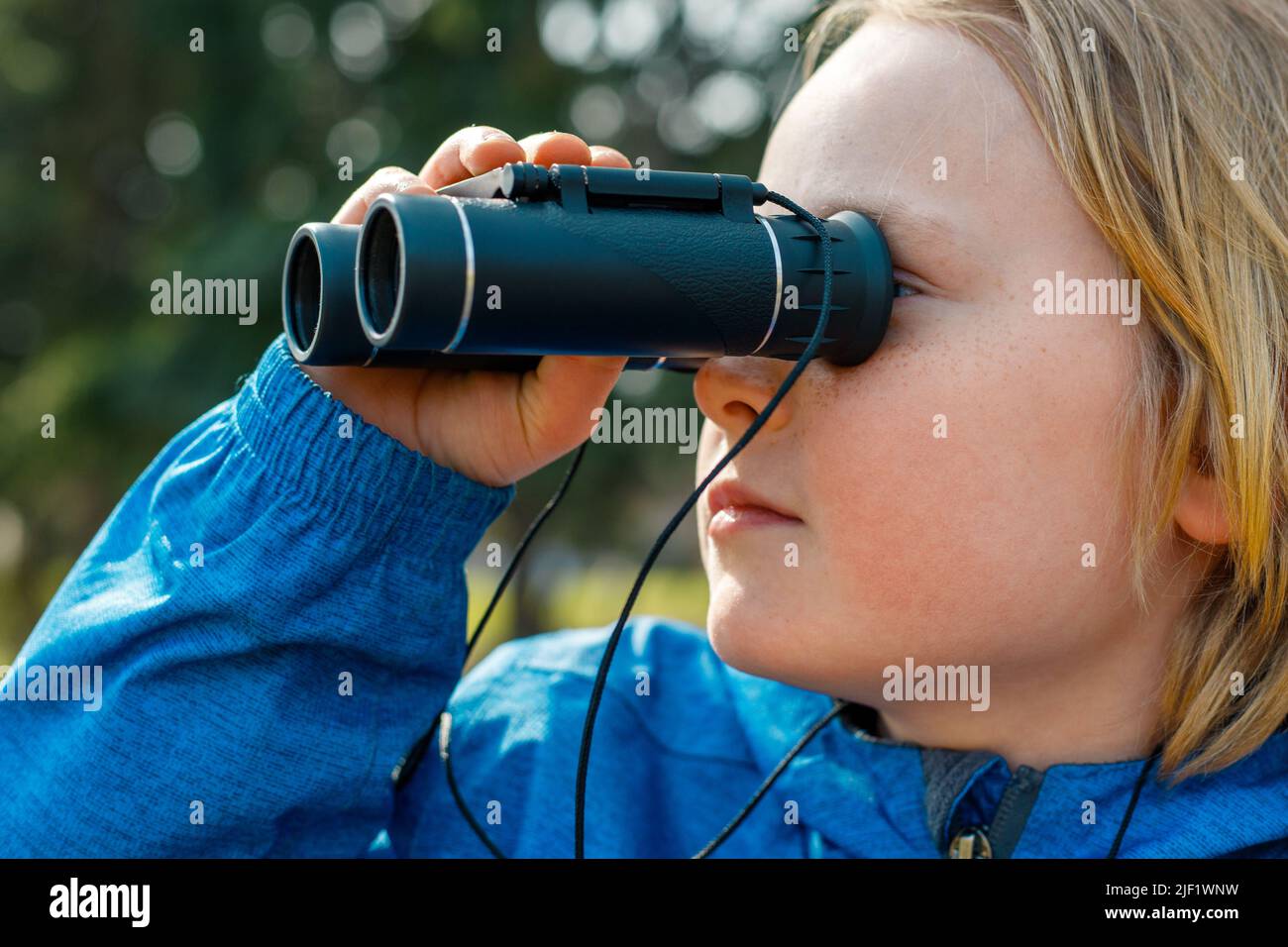 Enfant regardant à travers des jumelles dans le parc. Portrait en gros plan d'un garçon explorant la faune. Observation des oiseaux, randonnée et concept d'aventure. Banque D'Images