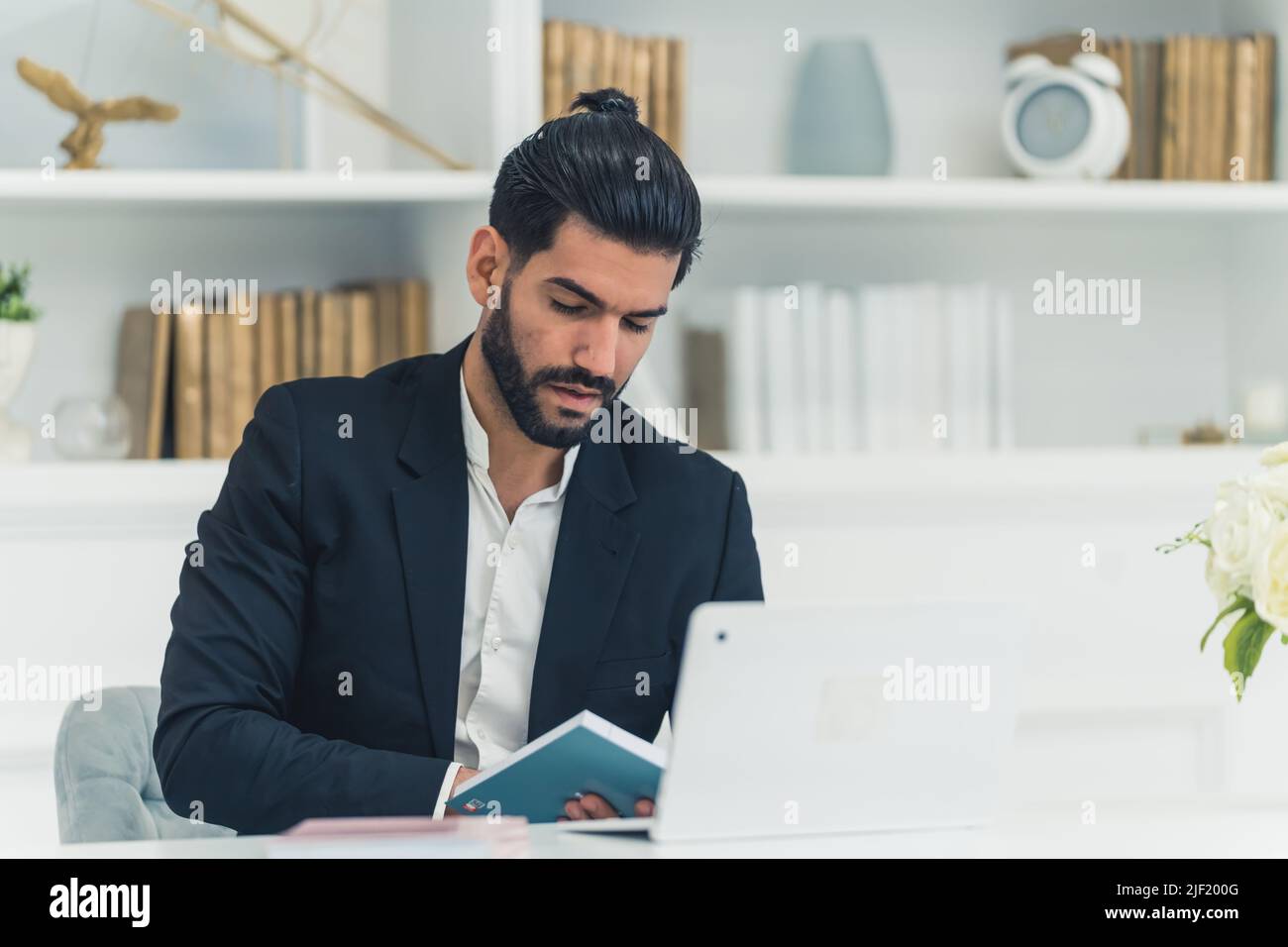 Cet homme latin à la barbe de 30s portait un élégant costume, assis devant un ordinateur portable et prenant des notes dans son ordinateur portable. Photo de haute qualité Banque D'Images