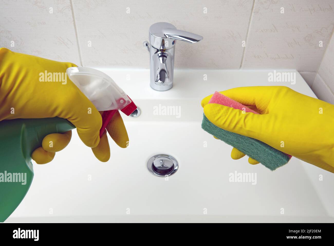 Les mains dans des gants de protection jaunes tiennent une éponge et un agent de nettoyage pour le nettoyage des équipements sanitaires dans la salle de bains Banque D'Images