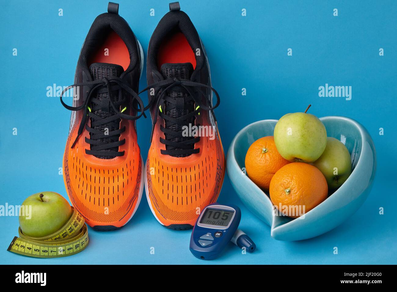 Baskets orange, glucomètre, mètre ruban et fruits dans un bol en forme de cœur sur fond bleu Banque D'Images