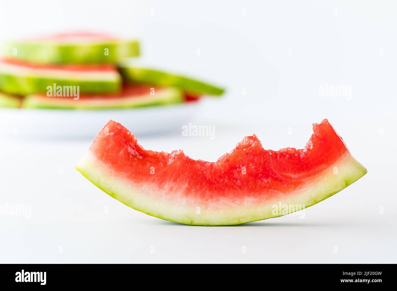 Une demi-tranche de pastèque mangée avec une pile de tranches de pastèque à l'arrière. Banque D'Images