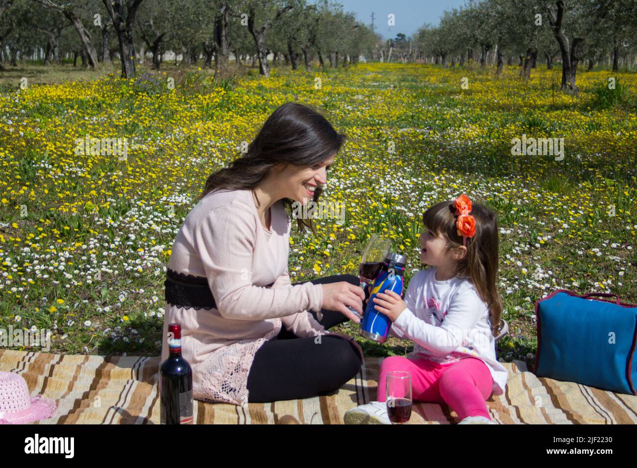 Photo d'une mère et de sa fille assises sur une couverture au milieu d'une prairie fleurie, car elles ont un pique-nique et un toast. Voyage de vacances en Toscane Banque D'Images