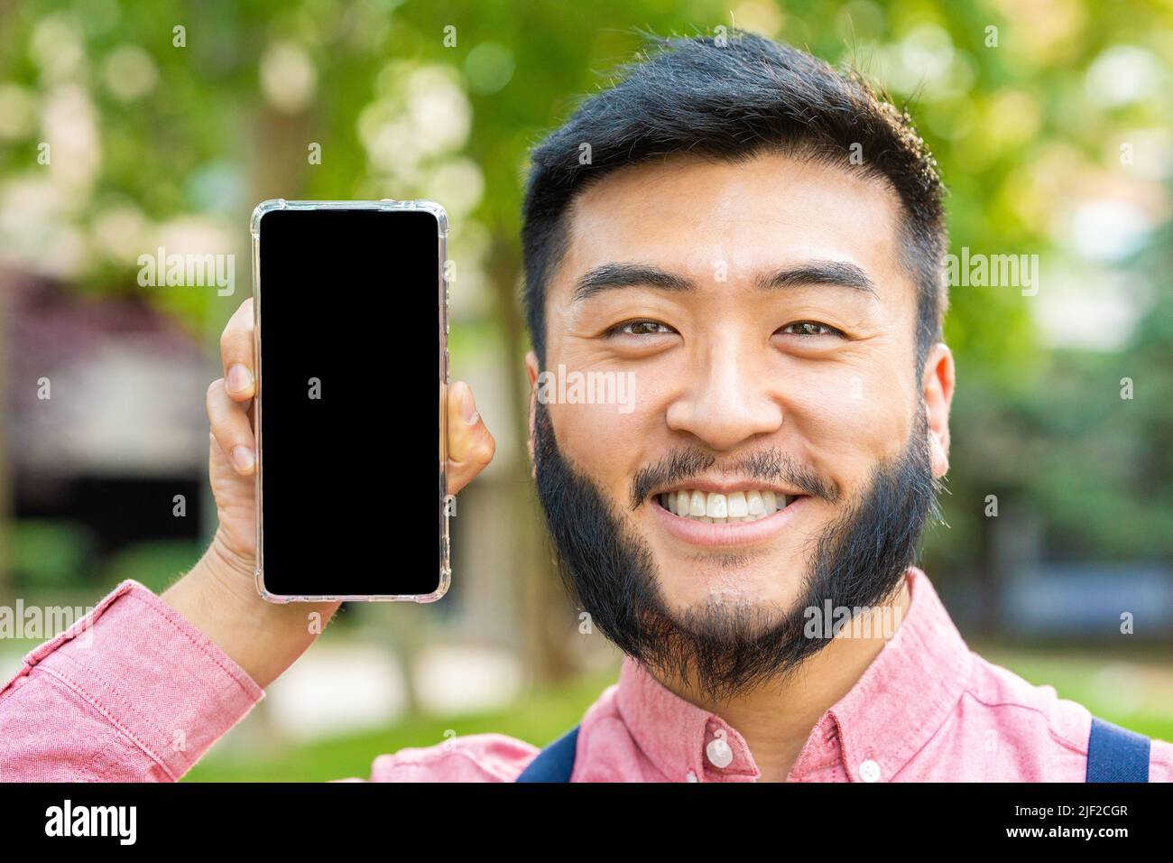 Homme asiatique montrant l'écran de téléphone mobile tout en souriant Banque D'Images