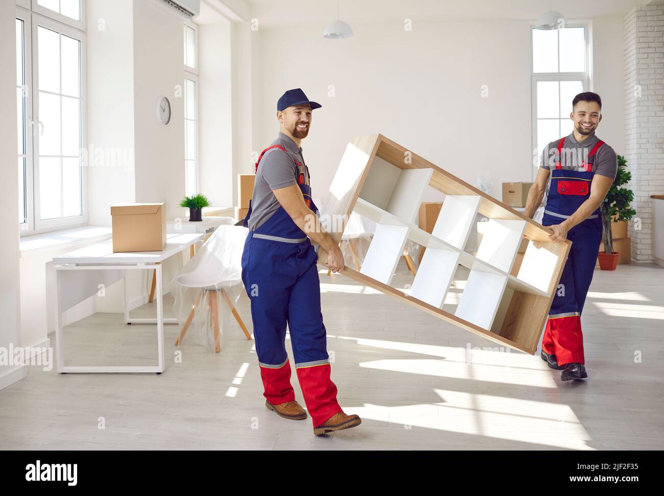 Équipe de travailleurs professionnels du service de déménagement dans les salopettes déplacer l'étagère dans l'appartement. Banque D'Images