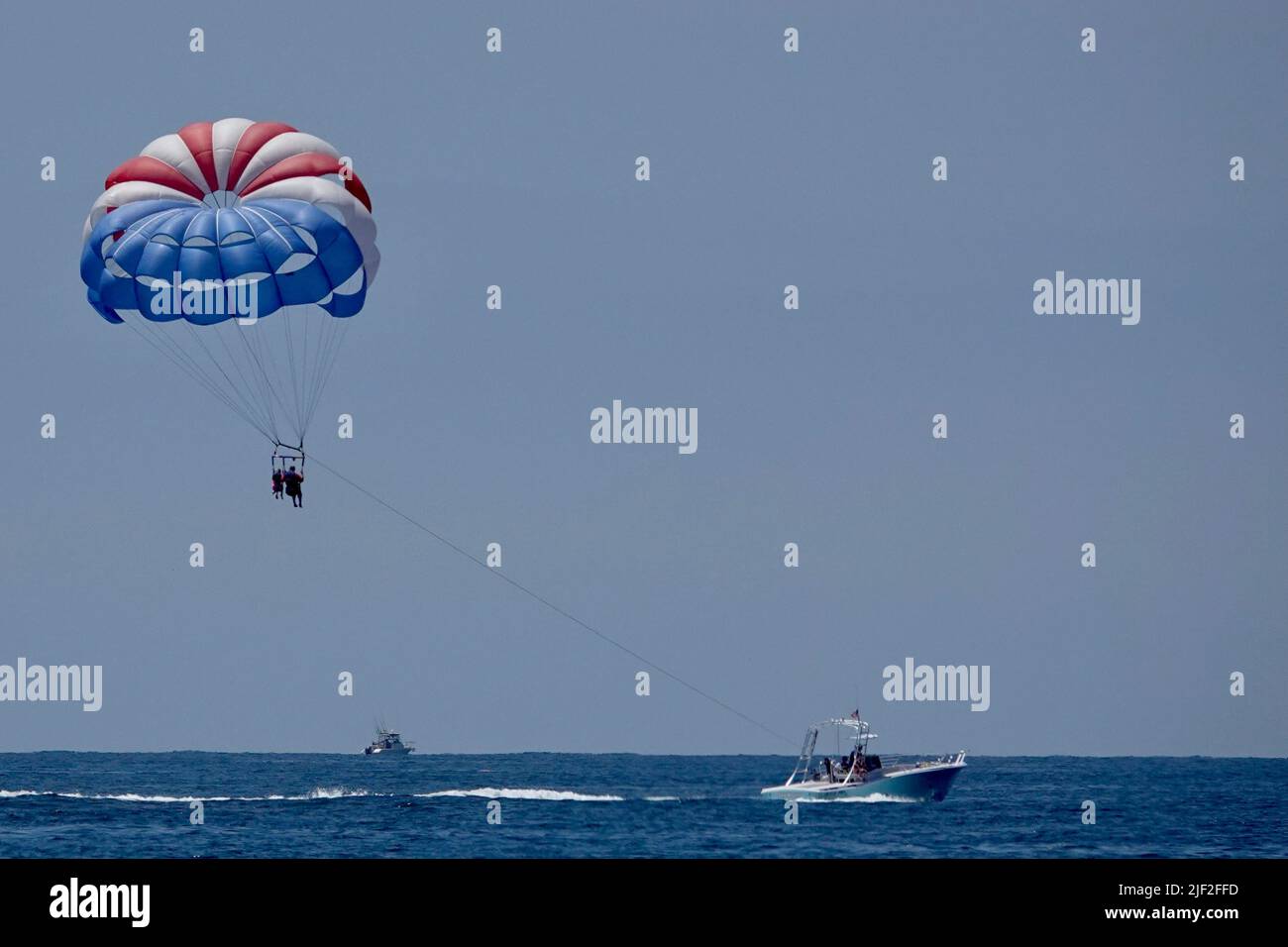 Une silhouette de deux personnes en parachute ascensionnel avec un parachute rouge, blanc et bleu au-dessus de l'océan. Banque D'Images