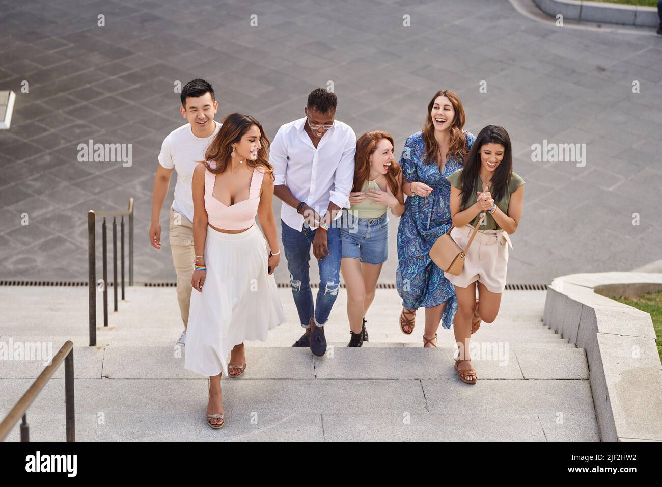 Groupe d'amis multiraciaux riant et bavardant en marchant dans les escaliers à l'extérieur. Amis portant des bracelets de drapeau LGBT. Diversité, amitié et concept LGBT. Banque D'Images