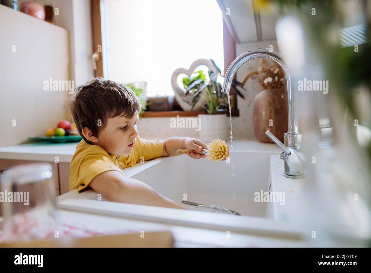 Petite tasse de lavage de garçon dans l'évier dans la cuisine avec gommage en bois, vie durable. Banque D'Images