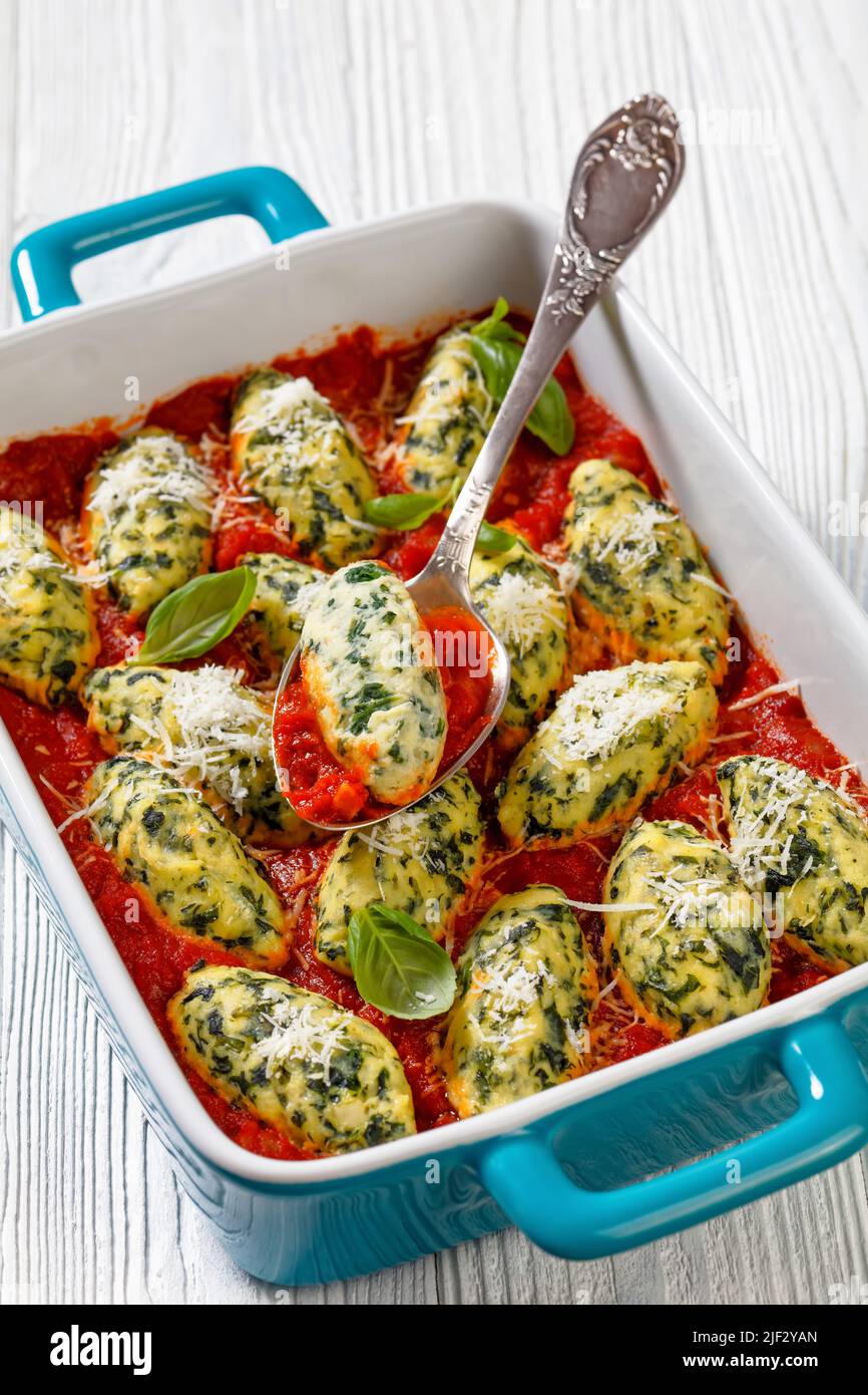 Boulettes de ricotta aux épinards italiens dans une sauce tomate aux herbes et parmesan râpé dans un plat de cuisson en céramique avec une cuillère Banque D'Images