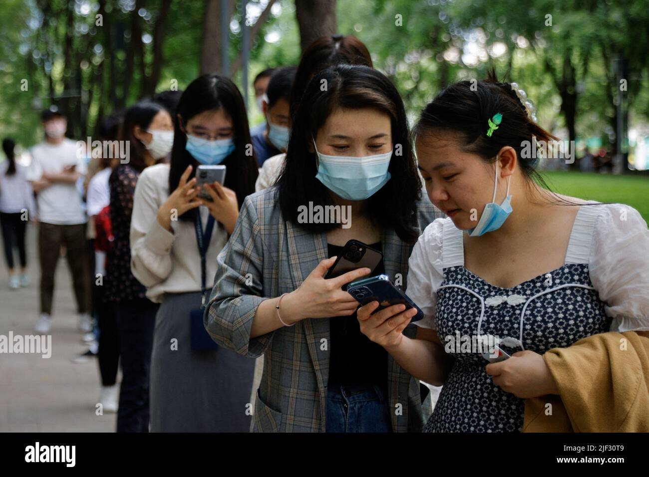 Les gens regardent leurs téléphones alors qu'ils se trouvent dans une station de test des acides nucléiques, à la suite d'une épidémie de coronavirus (COVID-19), à Beijing, en Chine, au 29 juin 2022. REUTERS/Thomas Peter Banque D'Images