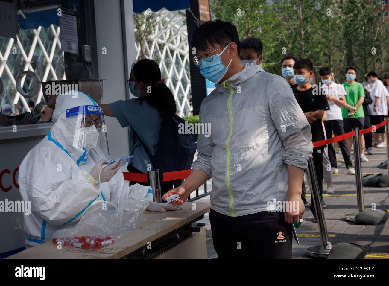 Un travailleur en costume protecteur scanne la carte d'identification d'un homme dans un poste de test d'acide nucléique, à la suite d'une épidémie de coronavirus (COVID-19), à Beijing, en Chine, au 29 juin 2022. REUTERS/Thomas Peter Banque D'Images