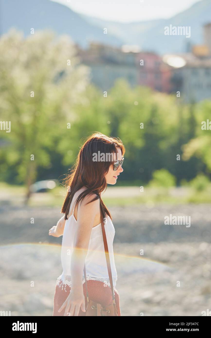 Bonne femme insouciante en vacances en profitant de la lumière du soleil marchant à côté d'une forêt. Femme insouciante appréciant ses vacances marchant dans la lumière du soleil par un Banque D'Images
