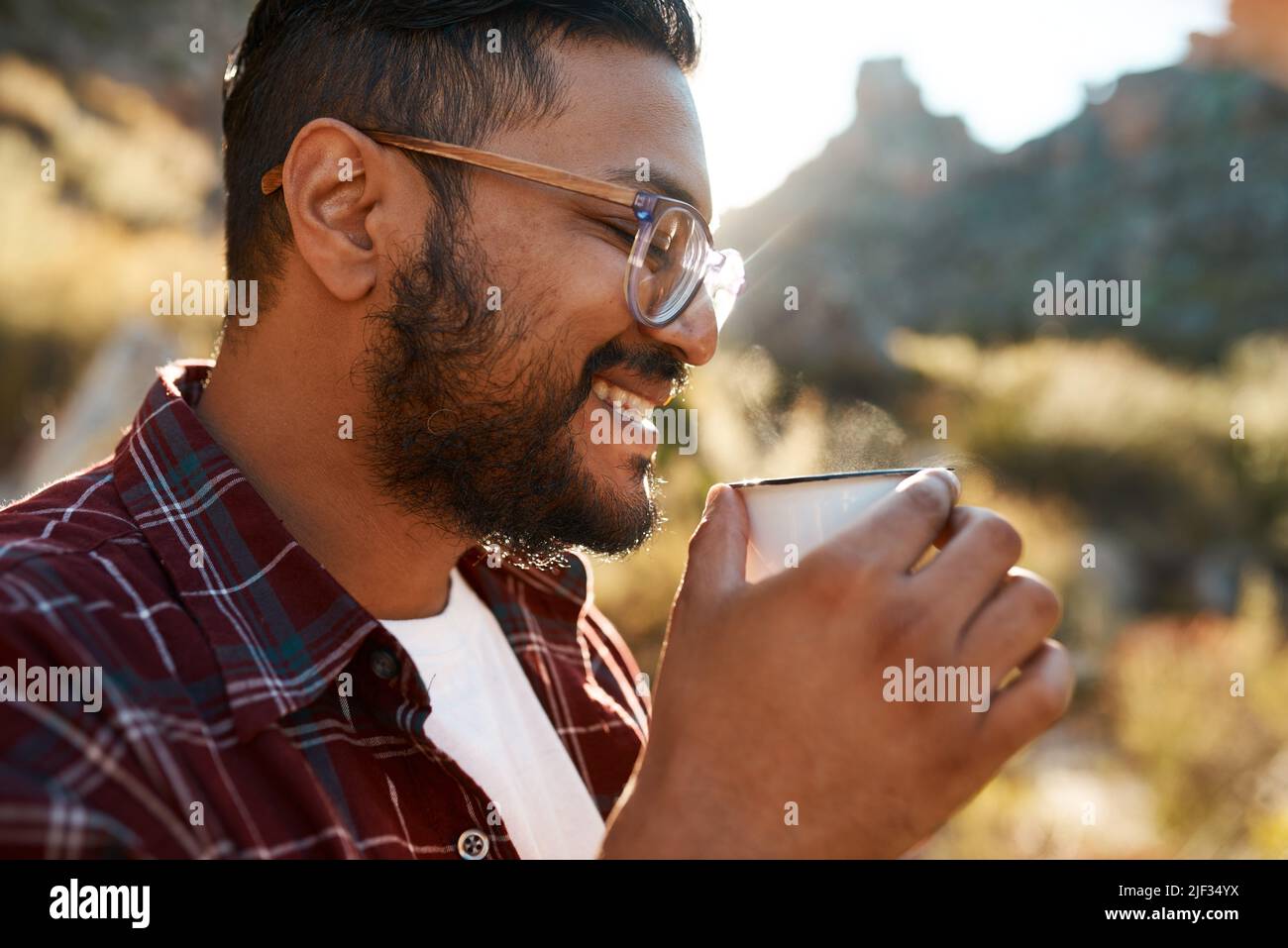 Un homme d'Asie du Sud sourit alors qu'il sourit un café lors d'un voyage en camping dans les montagnes Banque D'Images