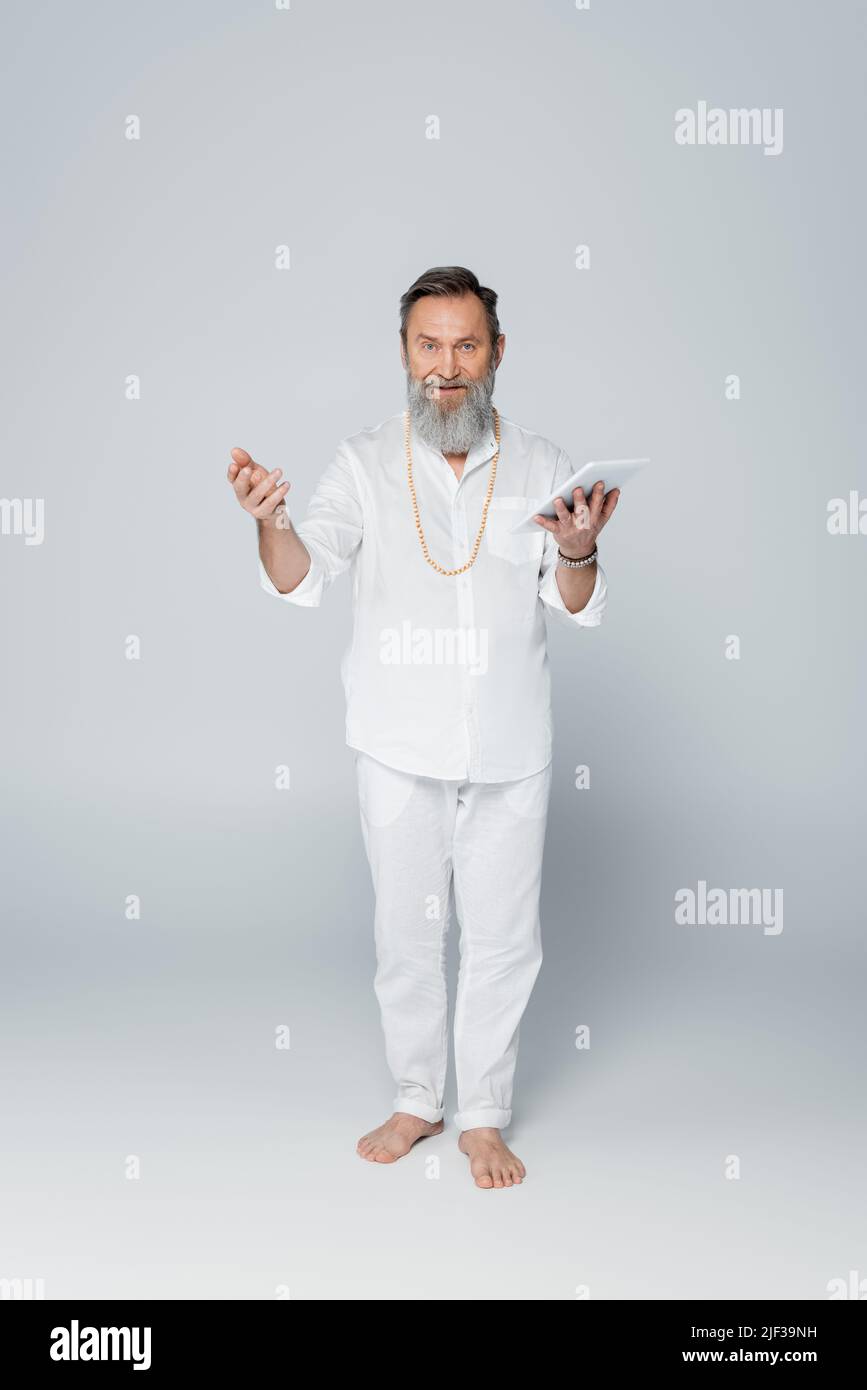 pleine longueur de gourou spirituel pieds nus tenant la tablette numérique sur gris Banque D'Images