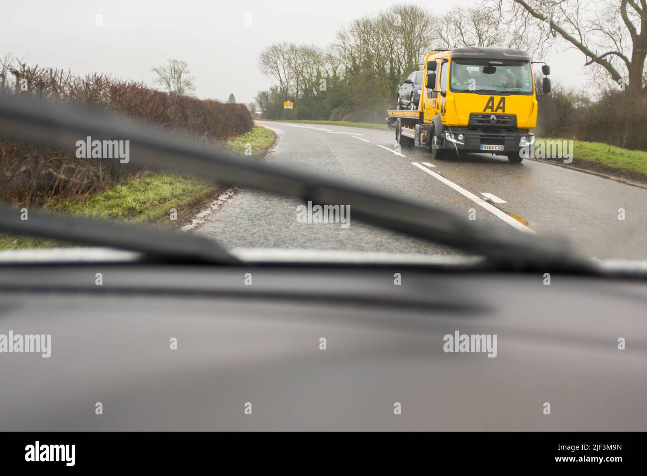Voiture chargée sur un camion de dépannage AA sur une route de campagne, vue du pare-brise d'une voiture arrivant en sens inverse, par temps pluvieux. Banque D'Images