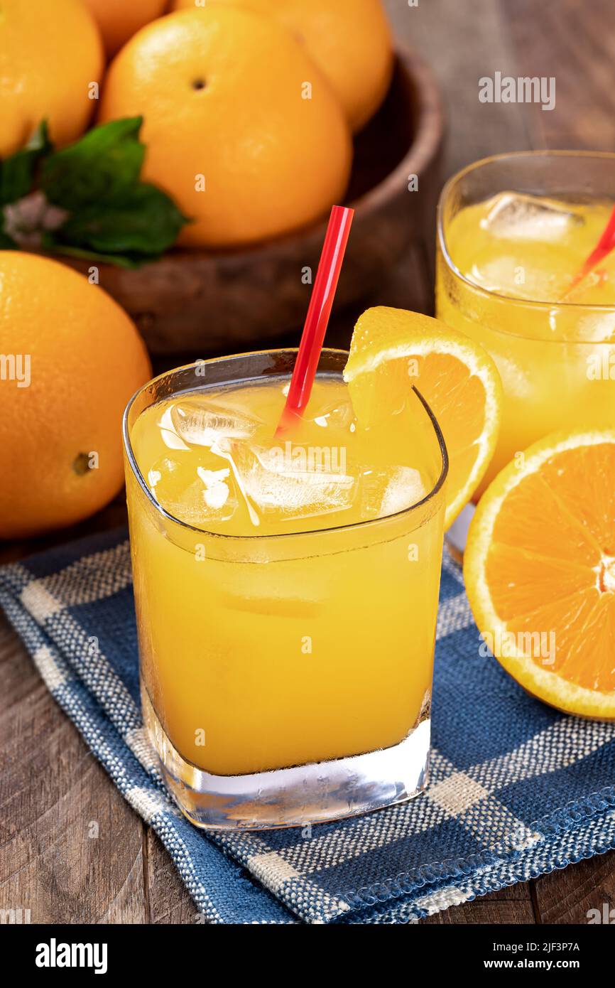 Un verre de jus d'orange froid et des oranges tranchées sur une table en bois avec un bol d'oranges en arrière-plan Banque D'Images