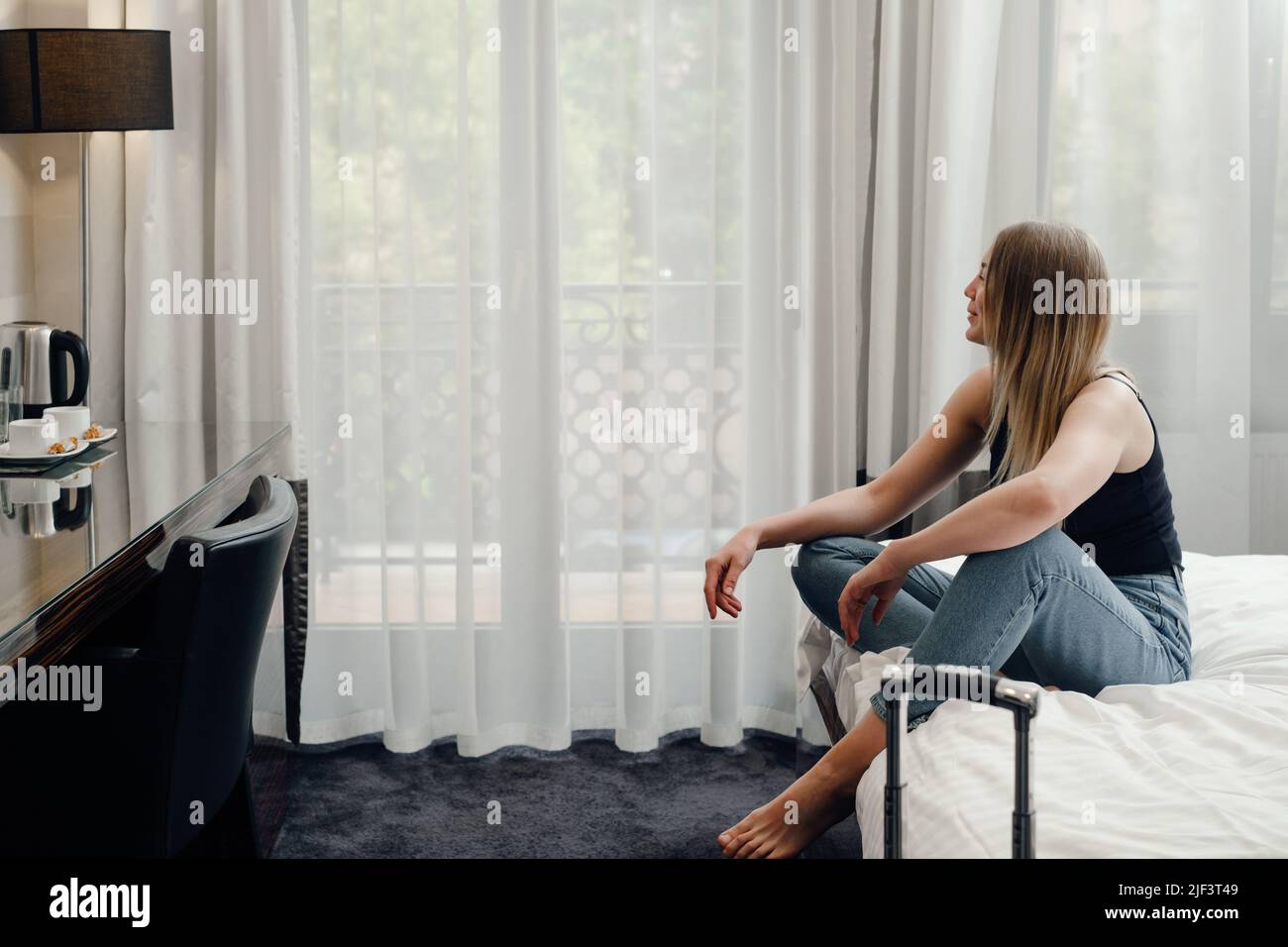 Jeune femme détendue dans la chambre d'hôtel lit regardant le smartphone, planification de la journée, Femme ayant le repos dans l'hôtel moderne pendant le voyage. Personne assise sur le Banque D'Images