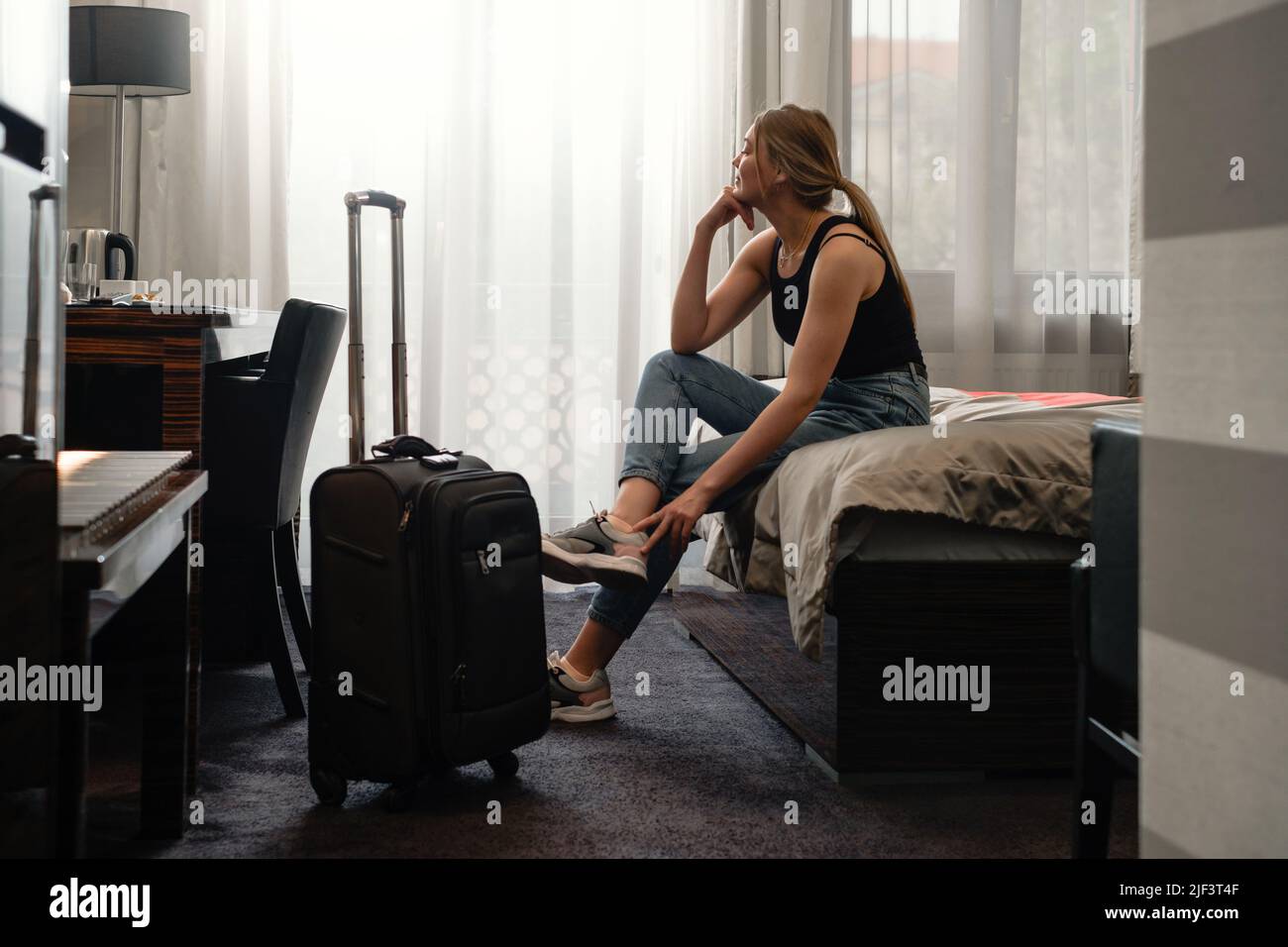 femme prenant des chaussures dans une chambre d'hôtel ensoleillée sur le lit. Touriste se détendre dans la chambre d'hôtel après avoir voyagé avec une valise. Bonne femme de se reposer Banque D'Images