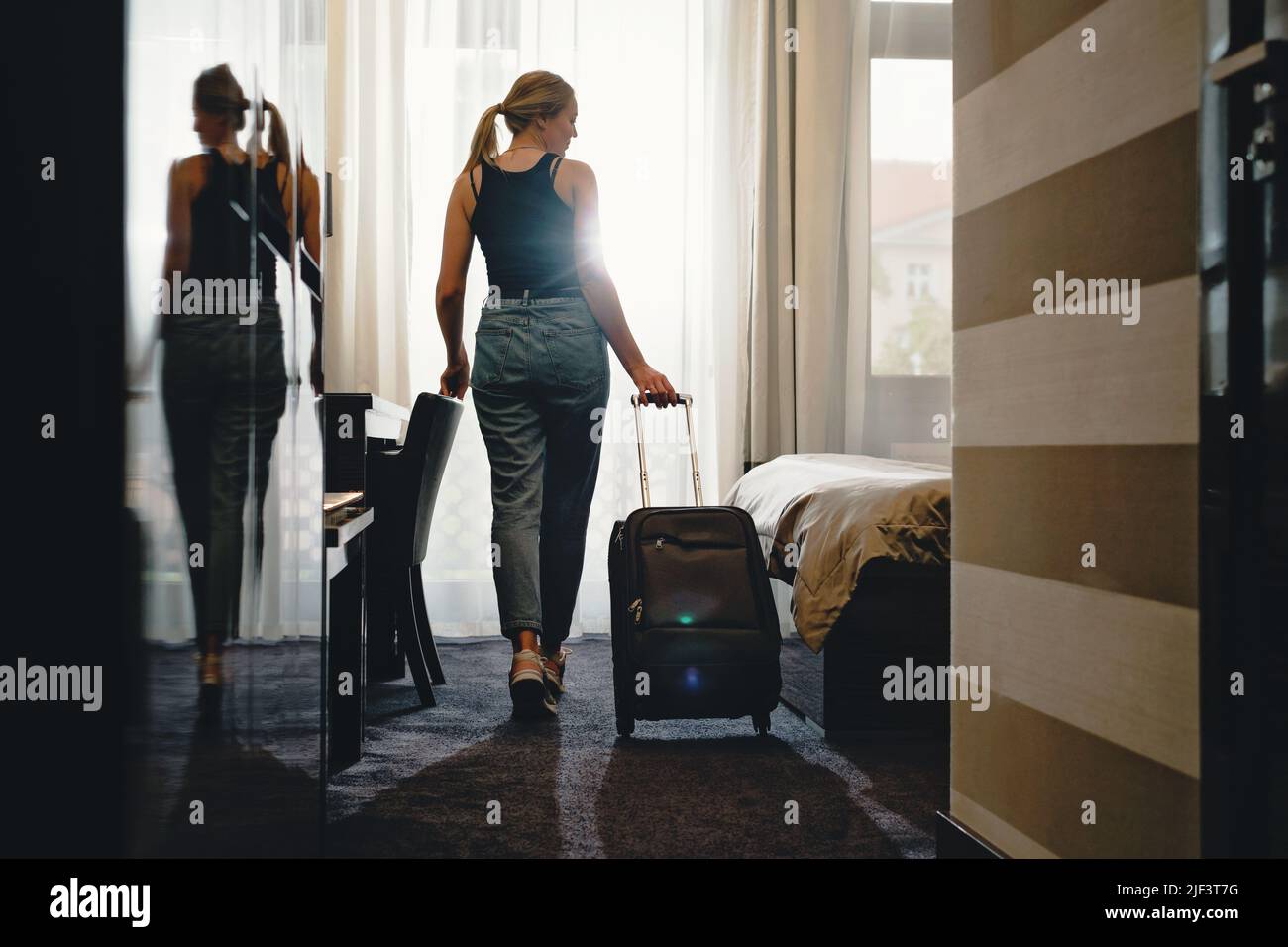 Femme voyageur avec une valise à bagages après l'enregistrement dans une chambre d'hôtel donnant sur la fenêtre. Silhouette de visiteur dans la personne d'hébergement de voyage Banque D'Images