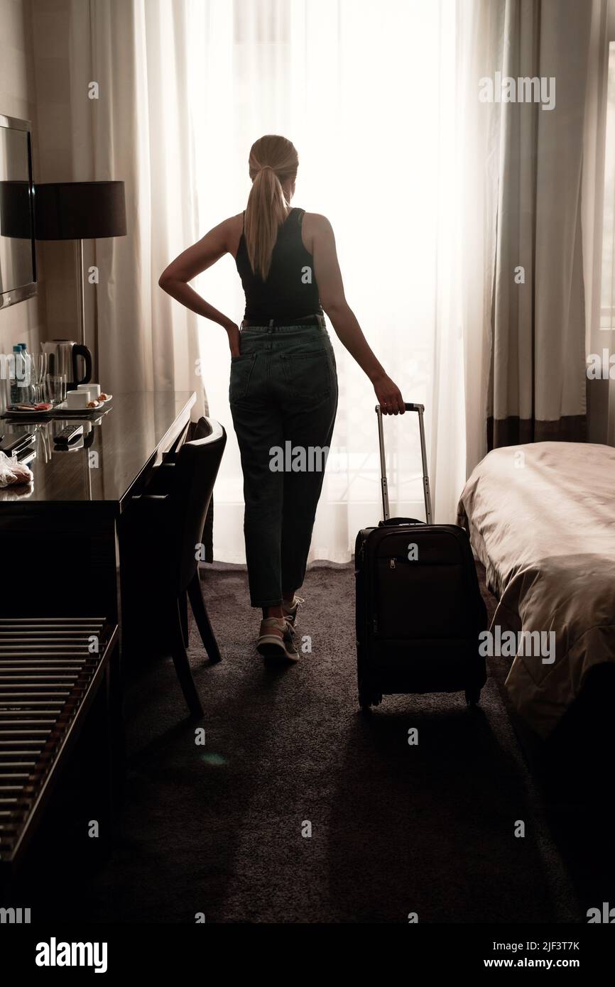 Femme voyageur avec une valise à bagages après l'enregistrement dans une chambre d'hôtel donnant sur la fenêtre. Silhouette de visiteur dans l'hébergement de voyage prêt à Banque D'Images