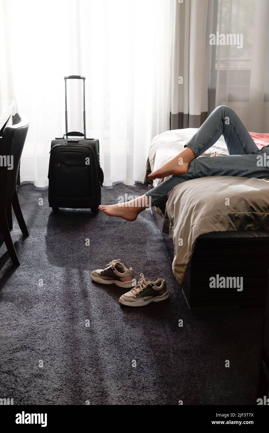 femme prenant des chaussures dans une chambre d'hôtel sur le lit. Touriste se détendre dans la chambre d'hôtel après avoir voyagé avec une valise. Femme ayant le repos après longtemps Banque D'Images