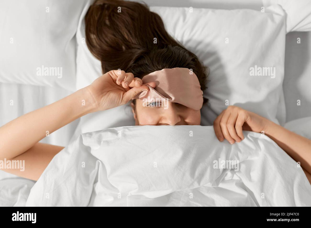 femme avec masque de sommeil oculaire dans le lit sous la couverture Banque D'Images