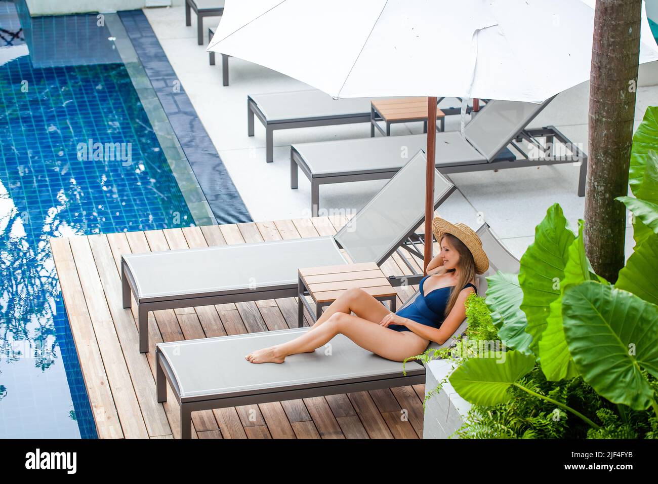 Jeune femme en maillot de bain allongé sur un salon près de la piscine, profitez de vacances d'été dans un complexe tropical. Femme voyage fille bain de soleil près de la piscine Banque D'Images
