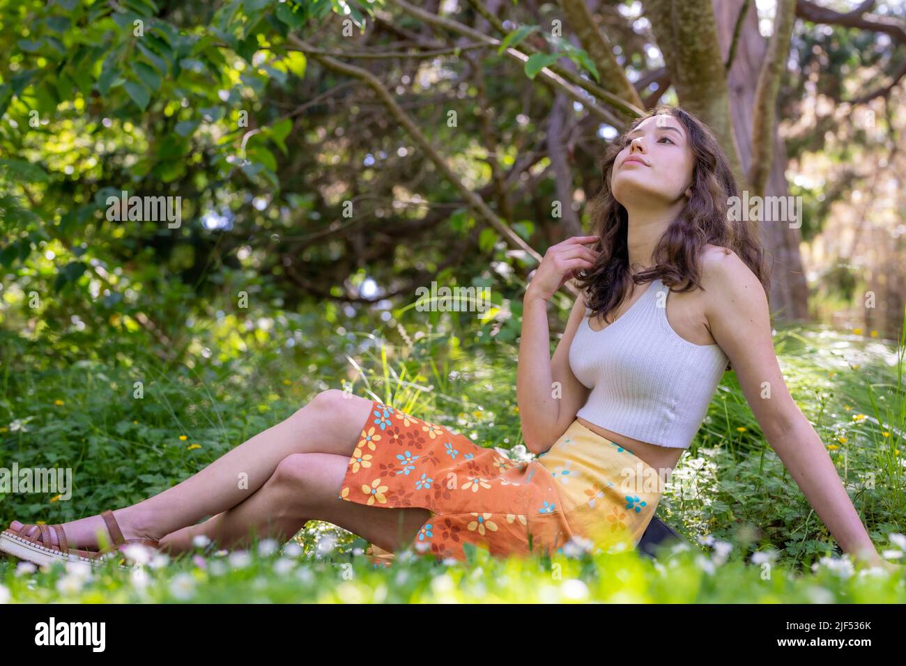 Portrait d'une jeune femme assise dans un jardin en jupe et brassière orange Banque D'Images