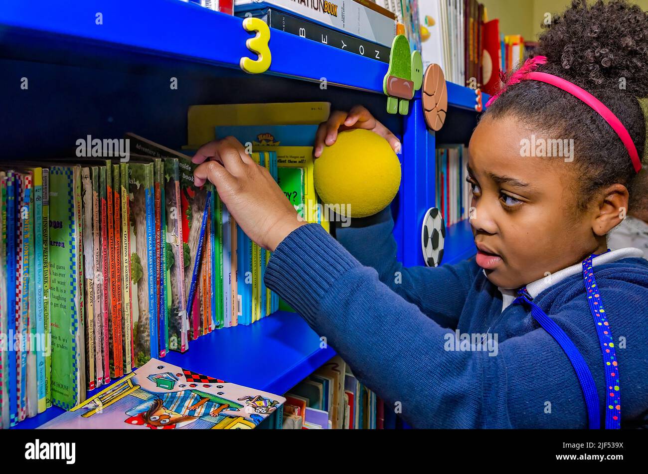 Une fille afro-américaine choisit un livre dans une bibliothèque lors d'un programme post-scolaire, le 28 février 2013, à Columbus, Mississippi. Banque D'Images