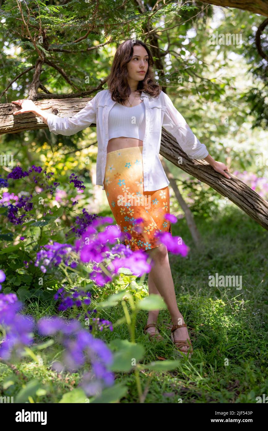 Jeune femme debout dans un jardin entouré d'arbres et de fleurs | Jupe à fleurs Banque D'Images